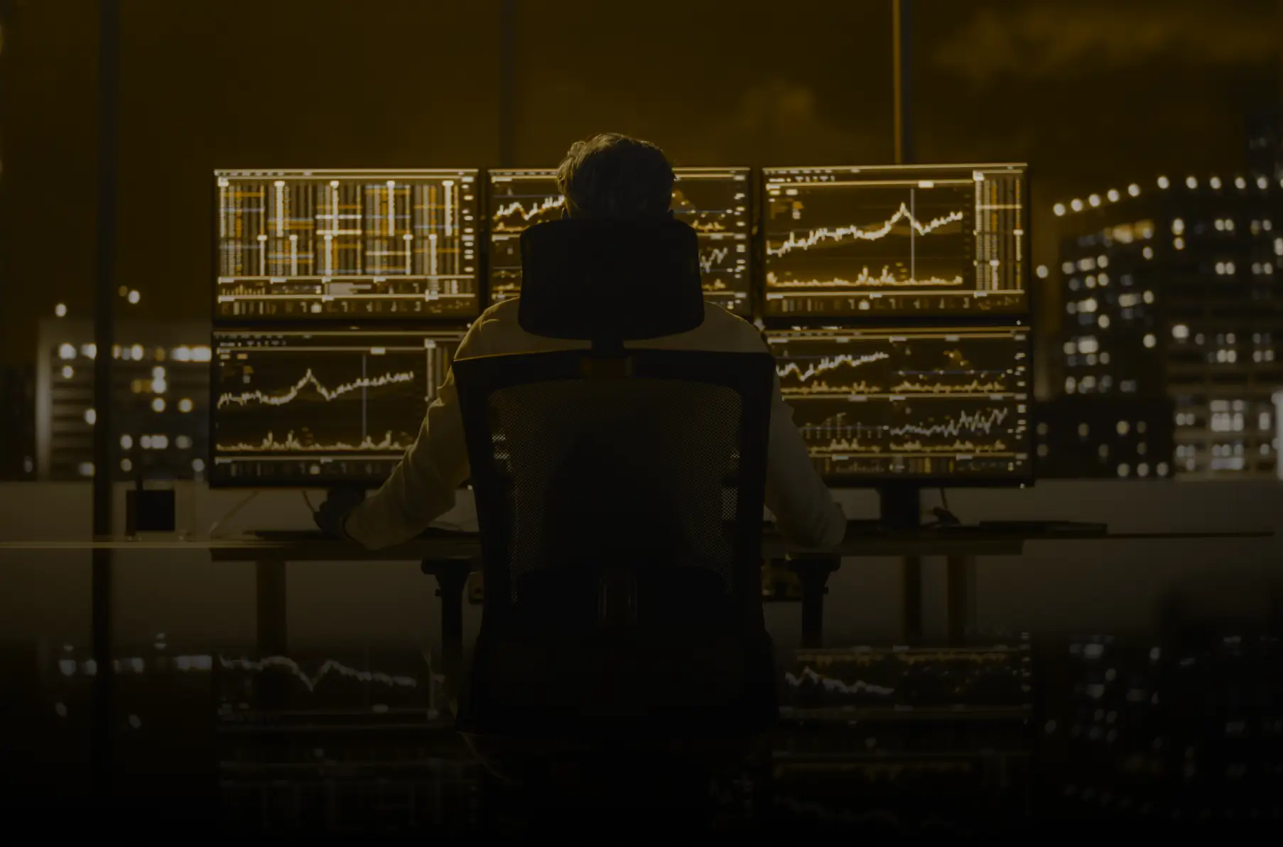 Person silhouetted against a wall of glowing trading monitors